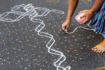 Unidentified indian woman seen drawing kolam (in tamil language) or rangoli using white colored rice during festival season