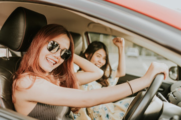 Young happy Asian girl best friends laughing and smiling in car during a road trip to vacation.