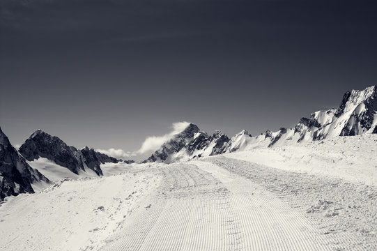 Fototapeta Black and white snowy road with trace from snow groomer