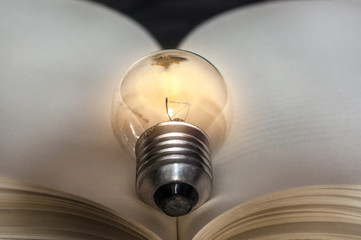 Yellow light bulb lamp over books, black background