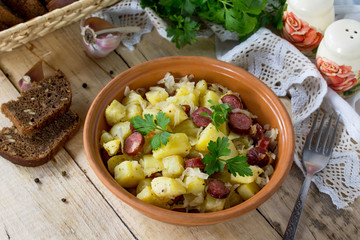 Homemade snacks on the kitchen wooden table in a rustic style. Warm salad with potatoes and smoked sausages.