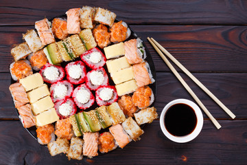 Tasty appetizing multicolored sushi rolls set on wooden table, served with soy sauce and chopsticks flat lay on wooden table. Sushi restaurant menu concept.