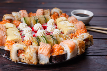 Tasty appetizing multicolored sushi rolls set, served with soy sauce and chopsticks on wooden table. Sushi restaurant menu, Japanese food, delicious seafood concept.