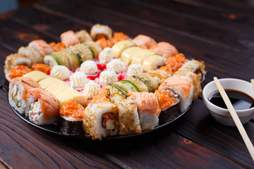 Tasty appetizing multicolored sushi rolls set, served with soy sauce and chopsticks on wooden table, selective focus