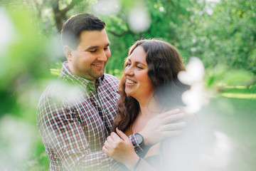 Obraz premium Young stylish happy couple in love hugging in blooming garden. Man and woman having romantic date outdoors.