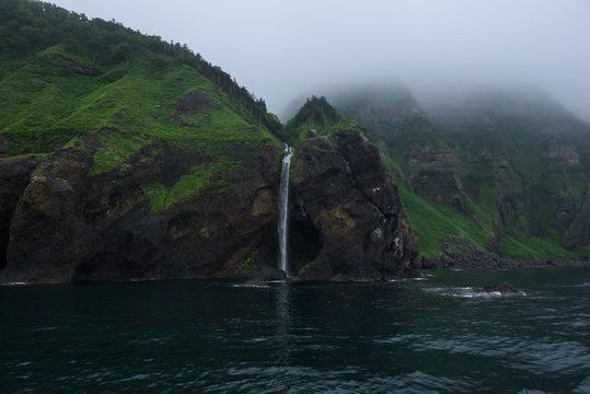 Waterfall dropping from high rocky cliffs into the ocean (Sea of Okhotsk) around the Shiretoko Peninsula, Hokkaido, Japan