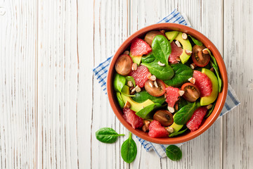 Fresh salad with spinach, avocado, tomatoes, grapefruit and almonds on white wooden background.