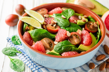 Fresh salad with spinach, avocado, tomatoes, grapefruit and almonds on white wooden background.