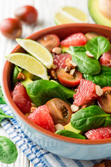 Fresh salad with spinach, avocado, tomatoes, grapefruit and almonds on white wooden background.