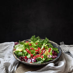 Green vegan salad in bowl with endive, arugula, mixed lettuces and pomegranate. Dieting, vegan food concept.