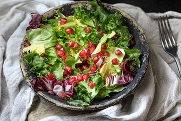 Green vegan salad in bowl with endive, arugula, mixed lettuces and pomegranate. Dieting, vegan food concept.