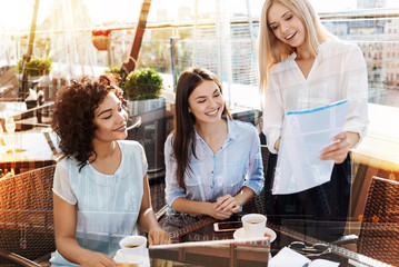 Warm atmosphere. Attentive females expressing positivity and looking at paper while sitting in cafe