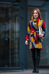 Full length portrait of cheerful female in colorful coat situating in street. Anticipation concept