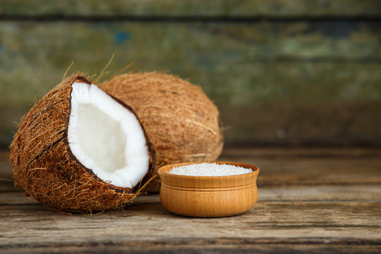 Fresh whole and cut in half coconuts with coconut flakes on wooden background with copy space