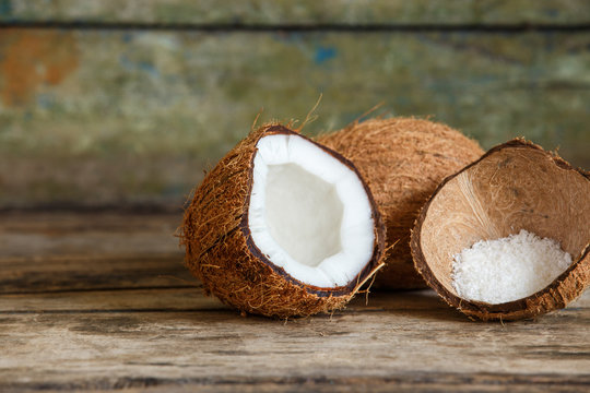 Fresh whole and cut in half coconuts with coconut flakes in shell on wooden background with copy space