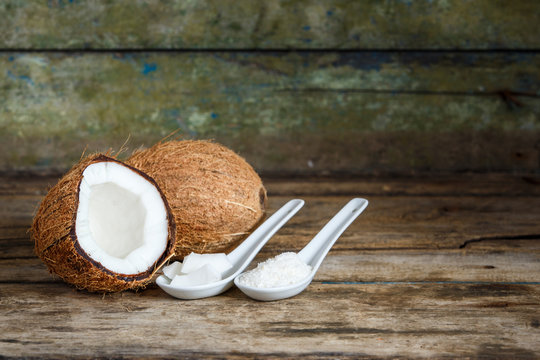 Fresh whole and cut in half coconuts with coconut flakes and shreds in spoons on wooden background with copy space