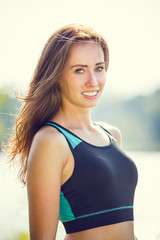 Portrait of young sporty woman resting after jogging in park near lake. Portrait of athletic girl in black top after fitness workout