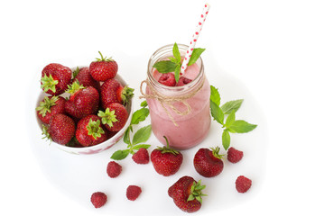 Pink strawberry and raspberry smoothie in a mason jar glass with straw and scattered berries