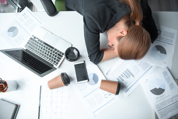 Top view serene weary female lying on desk in modern office. Mugs of beverage and different...