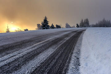 Obraz premium Wintertime - Black Forest. Winter landscape with road covered by snow and sun appearing in the background.