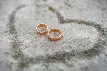 Obraz na płótnie Canvas Wedding rings for bride and groom on snow in shape of heart, marriage proposal in valentines day, winter wedding