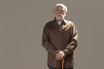 Waist up portrait of serious old man looking at camera with tranquility. Copy space in left side. Isolated on grey background