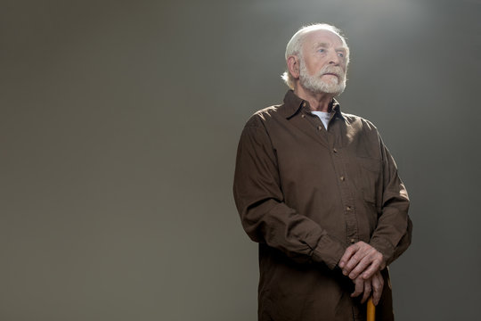 Elderly man with pensive face holding walking stick. Copy space in left side. Isolated on grey background