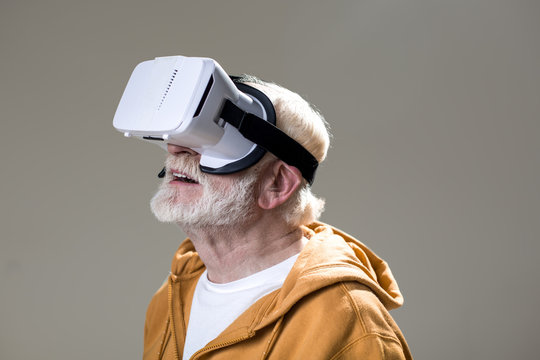 Enchanted Male Pensioner Having Fun While Using Virtual Googles. Isolated On Grey Background