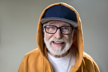 Portrait of bearded old man with hood dressed over the cap. His face expressing positivity....