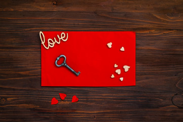 red envelope with hearts and a key on a wooden background, the concept of Valentine's Day, top view