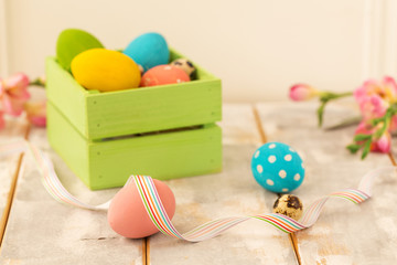 Multicolored Easter eggs in a wooden box, ribbons and flowers on a wooden background. Country style.