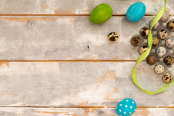 Multicolored Easter eggs in plastic box and ribbons on a wooden background. Country style. Flat lay. Space for text