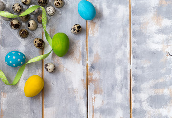 Multicolored Easter eggs in plastic box and ribbons on a wooden background. Country style. Flat lay. Space for text