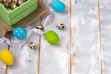 Multicolored Easter eggs in a wooden box, ribbons on a wooden background. Country style.