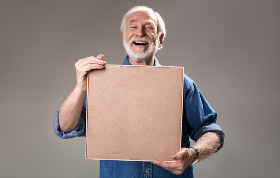 Laughing mature man carrying wooden cadre in front of him. Isolated on grey background