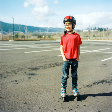 Eight year old boy on roller blades in an empty parking lot on a sunny day