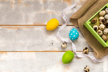 Multicolored Easter eggs in a wooden box, ribbons on a wooden background. Country style. Flat lay. Space for text.