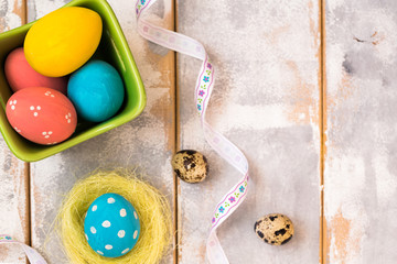 Multicolored Easter eggs in a wooden box and ribbons on a wooden background. Country style. Flat lay