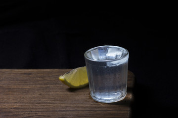 Vodka shot with lemon and ice on wooden deck and dark background