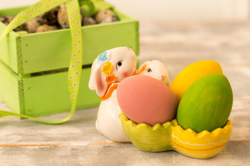 Multicolored Easter eggs in a wooden box, rabbit, ribbons on a wooden background. Country style.