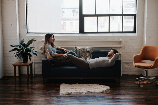 Attractive young interracial couple cuddling on couch in trendy loft apartment