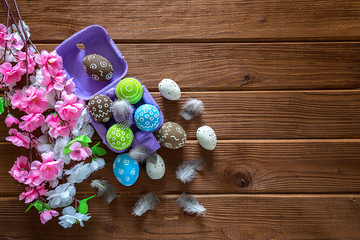 Painted Easter eggs with feathers and a branch of sakura on a dark wooden background