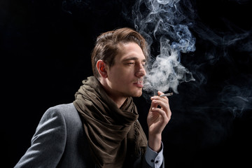 Sadness. Side view of pensive young stylish man is standing and enjoying cigarette. He is looking...