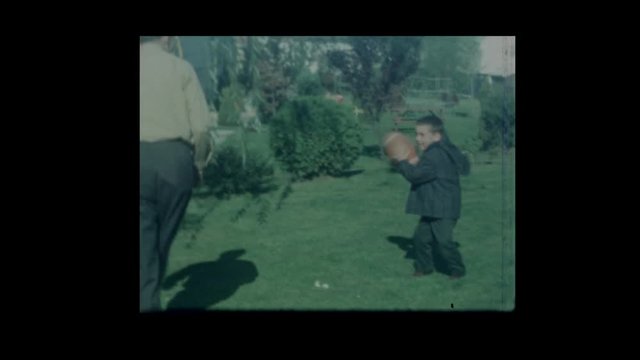 1966  Father tosses football with sons in backyard