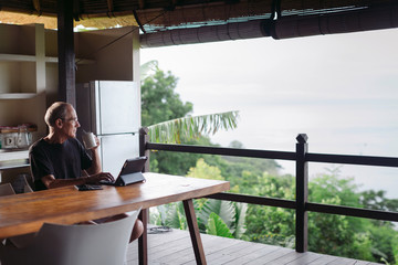 Mature man in his 60's working and traveling with tablet in trop