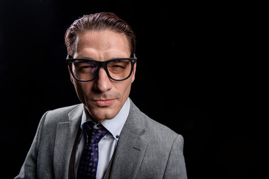 Portrait of young distrustful businessman in glasses is standing in suit. He is squinting his eyes while looking at camera suspiciously. Isolated background with copy space in the right side