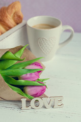 Cup of coffee with croissants, bouquet of pink tulips and wooden word LOVE