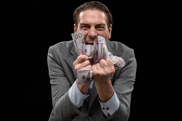 Passion about money. Portrait of adult crazy manager is standing and squeezing dollars in his fists...