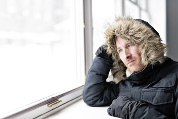 Man With Warm Clothing Feeling The Cold Inside House close to a window