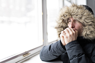 Man With Warm Clothing Feeling The Cold Inside House close to a window